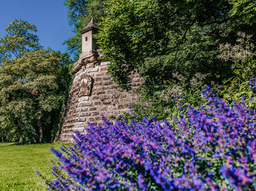 Wachtürmchen der Festungsanlage mit blauen Blumen im Vordergrund sowie Bäumen und Rasen im Stadtpark