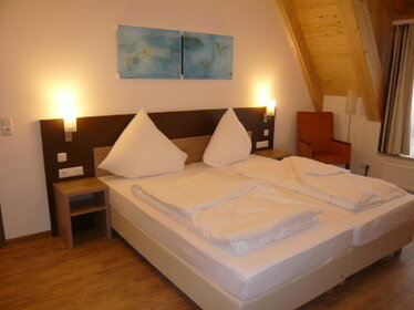 Doppelbett mit weißer Bettwäsche, eingeschaltete Nachttischlampen und blauem Bild an der Wand