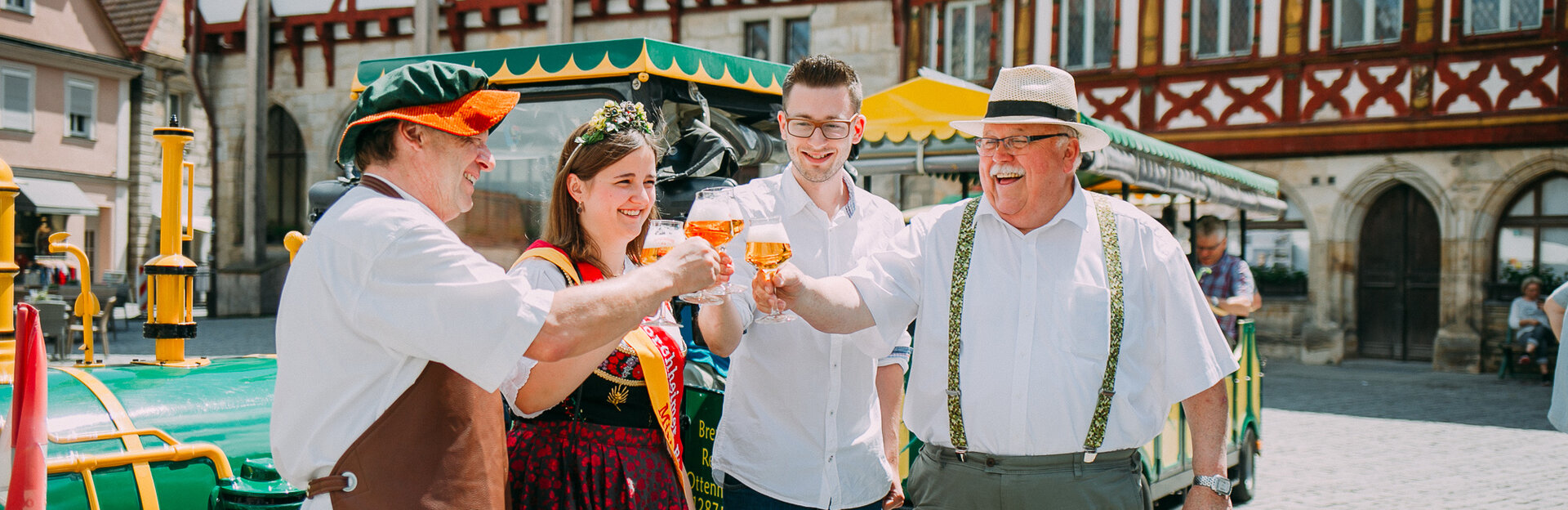 Bierkönigin und drei Männer stoßen mit Bierkrügen vor dem Fachwerk-Rathaus an