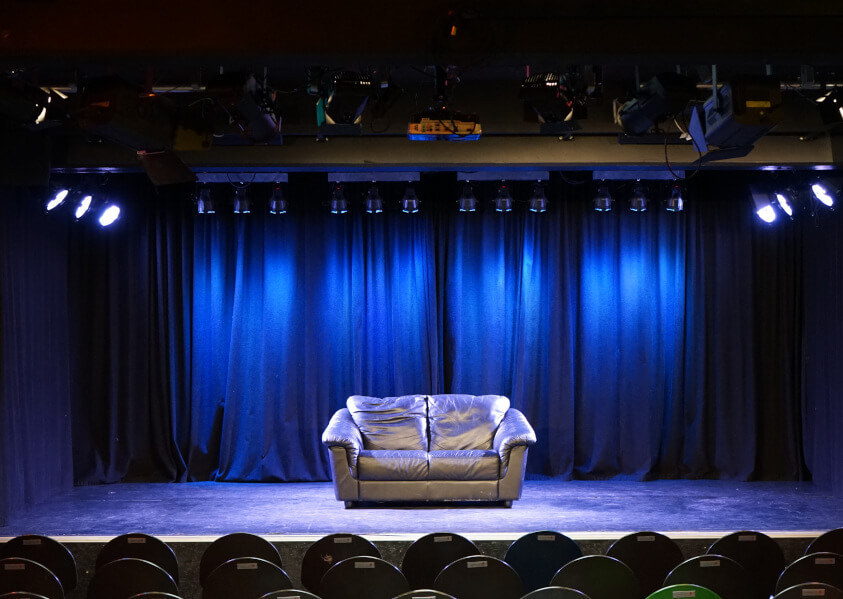 Junges Theater mit Sofa auf Bühne in blauem Licht