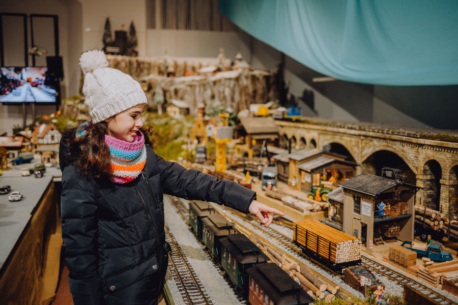 Mädchen mit Wintermantel und Wollmütze zeigt auf die Modelleisenbahn im Pfalzmuseum
